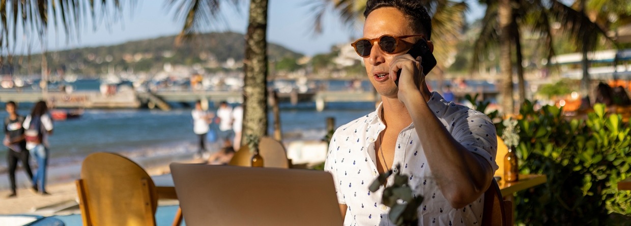 Zakenman zit op het strand achter zijn laptop en is aan het bellen